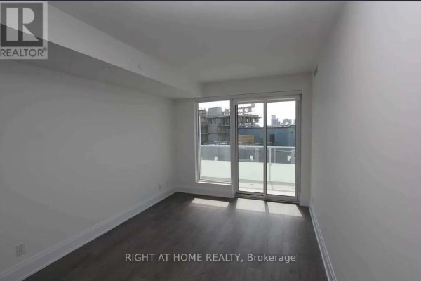 Empty room with dark wood flooring and sliding glass doors opening to a balcony. - 413 - 20 Brin Drive, Toronto