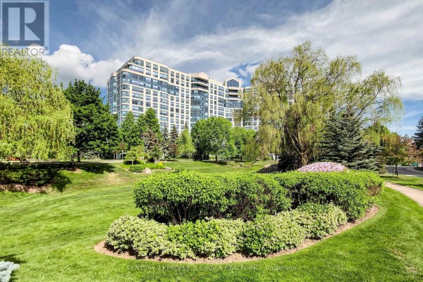Lush green landscaping and trees in front of a multi-story beige apartment building. - #413 - 7805 Bayview Avenue, Markham
