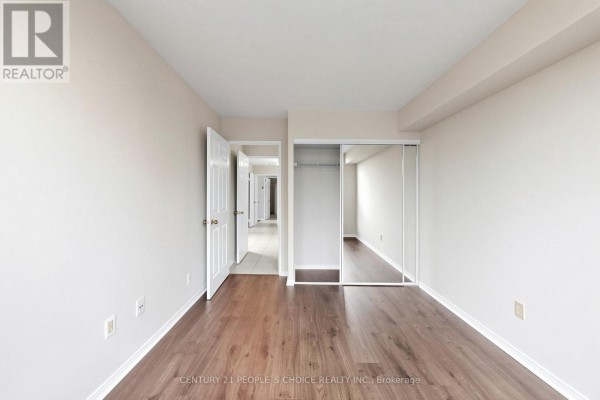 Bedroom with dark wood laminate flooring, white walls, and a closet with mirrored doors. - #413 - 7805 Bayview Avenue, Markham