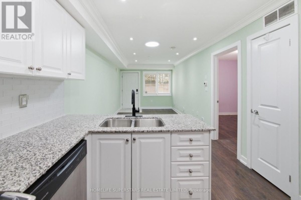Kitchen counter with a double sink and faucet, white cabinets, and a doorway to a bedroom. - 413 - 8 Drummond Street, Toronto