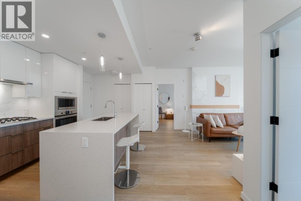 Living room with sectional sofa, modern entertainment unit, and open kitchen area. - 413 11641 227 Street, Maple Ridge
