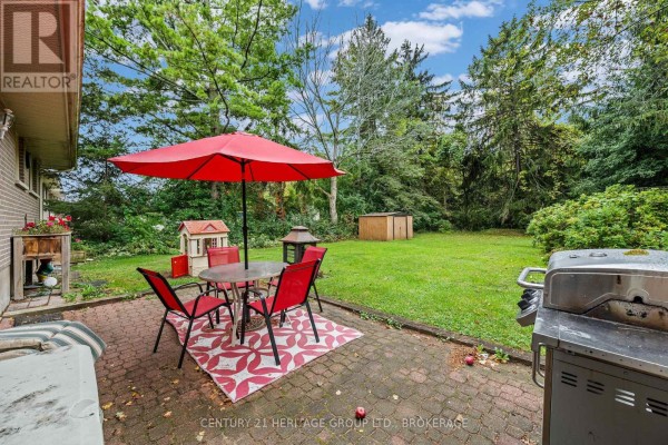 Backyard patio with red chairs, umbrella, grill, and a children's playhouse. - 413 Maple Ridge Drive, Kingston