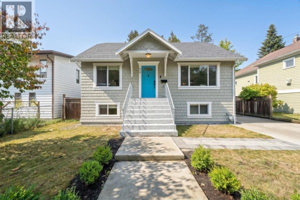 Front exterior of a grey house with a bright blue front door and a white staircase. - 413 Seventh Avenue, New Westminster