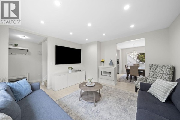 Living room with blue sofas, a white fireplace, and a dining area visible through an opening. - 413 Seventh Avenue, New Westminster