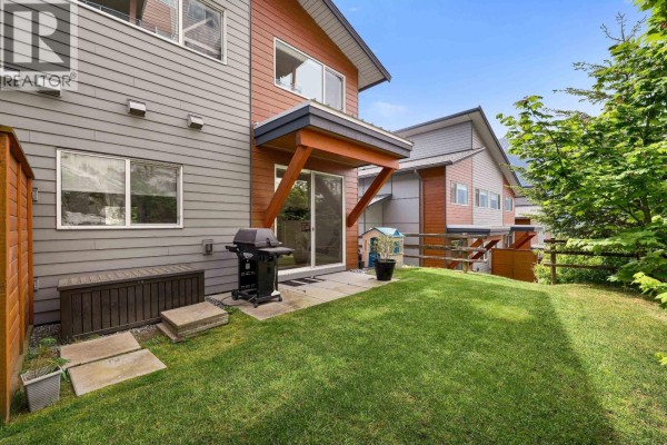 Side view of a duplex backyard with a lawn, sliding glass door, and storage. - 41322 Horizon Drive, Squamish