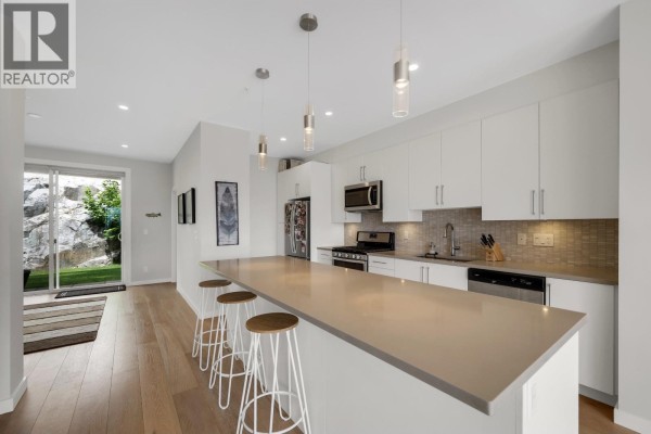 Modern kitchen with white cabinets, grey countertops, and a large island with stools. - 41322 Horizon Drive, Squamish