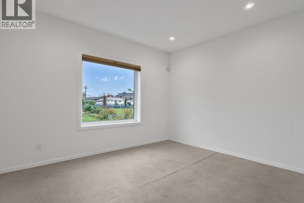 Empty bedroom with white walls, a large horizontal window, and grey carpet. - 4136 Beatrice Street, Vancouver