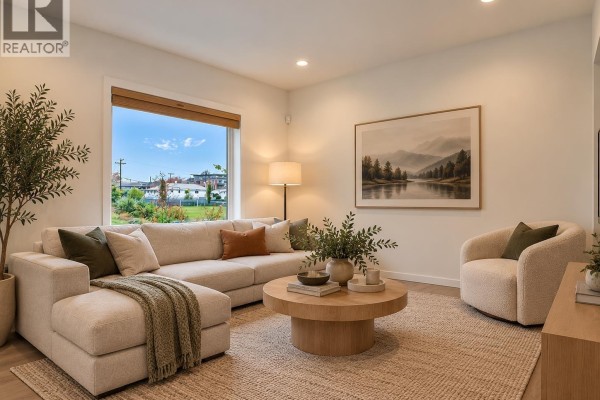 Living room with sectional sofa, round coffee table, and large window view. - 4136 Beatrice Street, Vancouver