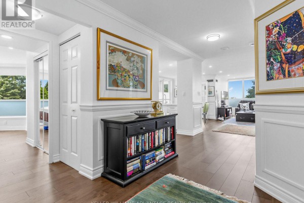 Hallway with dark wood floors, white walls, a large mirrored closet, and artwork. - 414 - 20 Guildwood Parkway, Toronto