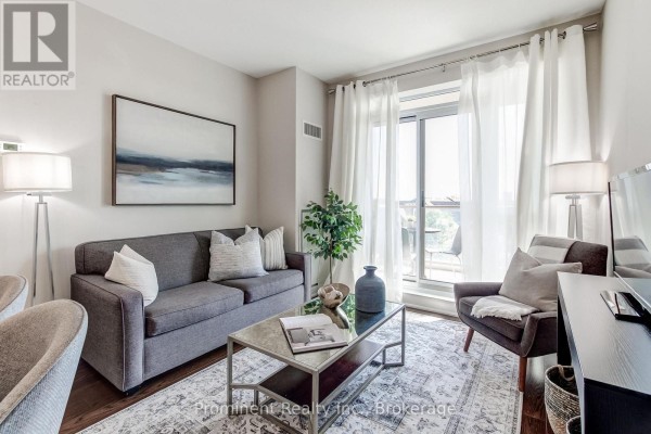 Living room with grey sofa, armchair, coffee table, and white curtains covering a sliding glass door. - 414 - 2470 Prince Michael Drive, Oakville