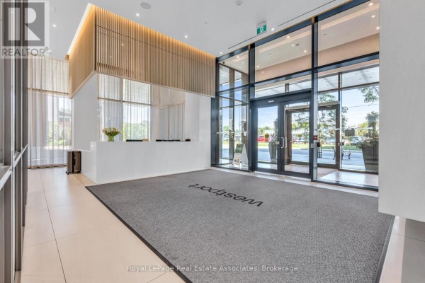 Modern lobby with a white reception desk, wood accents, and large glass doors. - 414 - 28 Ann Street, Mississauga