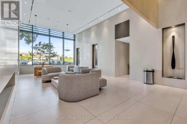 Spacious lobby seating area with grey sofas, a coffee table, and large windows. - 414 - 28 Ann Street, Mississauga