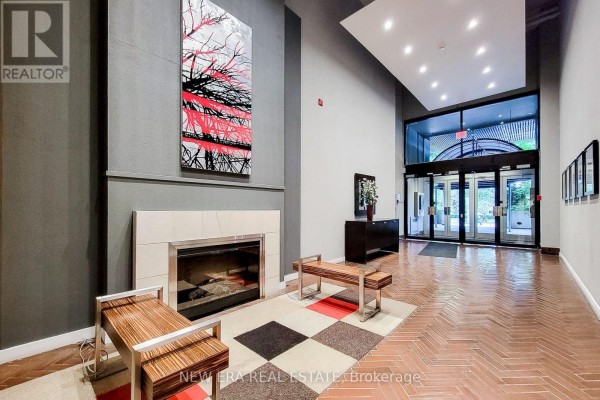 Apartment building lobby with a fireplace, two wood benches, abstract art, and entrance doors. - 414 - 66 Bay Street S, Hamilton