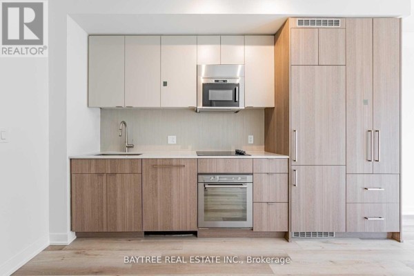 Close-up of a modern kitchen featuring light wood cabinetry, stainless steel oven, and microwave. - 414 - 840 St Clair Avenue W, Toronto