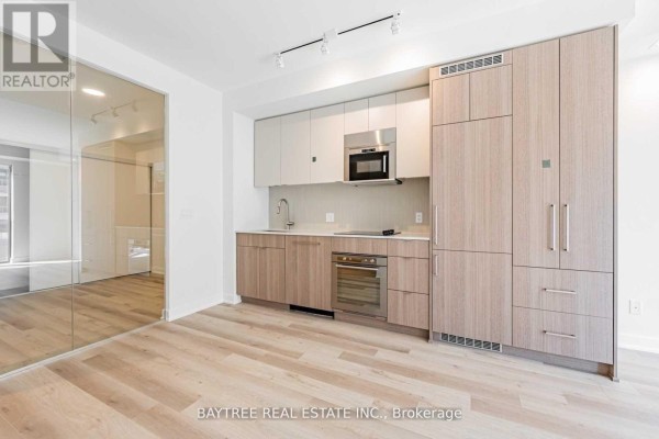 Kitchen and dining area with light wood cabinetry, stainless steel appliances, and glass partition. - 414 - 840 St Clair Avenue W, Toronto