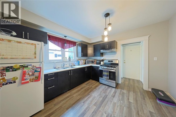 Kitchen with dark cabinets, white countertops, stainless steel gas stove, and wood-look flooring. - 414 Davis Street, Sarnia