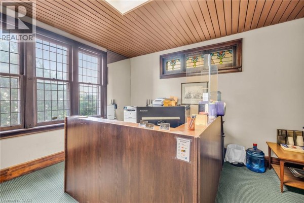Reception desk with a wooden counter, printers, computer, and stained glass window. - 414 Main Street E, Hamilton