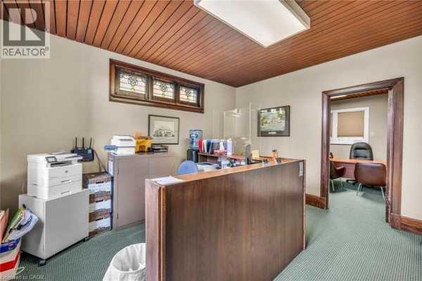 Office reception area with a wooden desk, printers, water cooler, and doorway to another office. - 414 Main Street E, Hamilton
