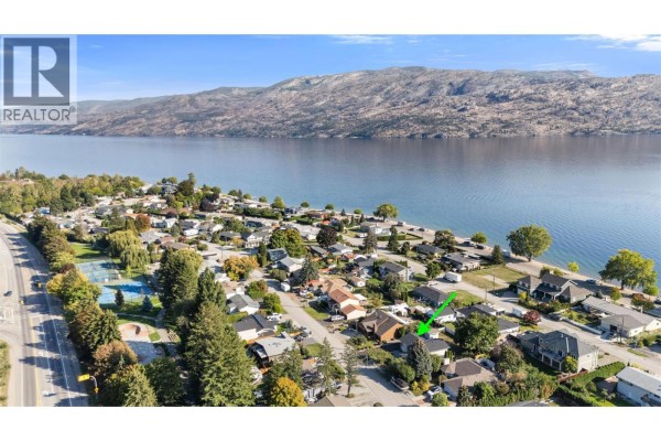 Aerial view of a residential neighborhood with houses and trees bordering a large blue lake and mountains. - 4141 San Clemente Avenue, Peachland