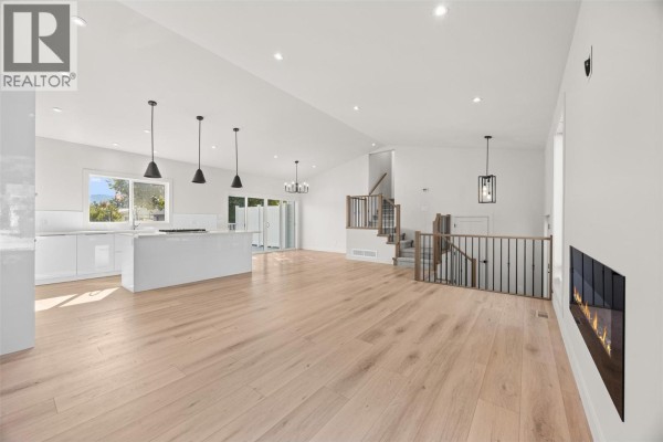 Open concept living area with white kitchen cabinets, island, light wood floors, and a modern fireplace. - 4141 San Clemente Avenue, Peachland