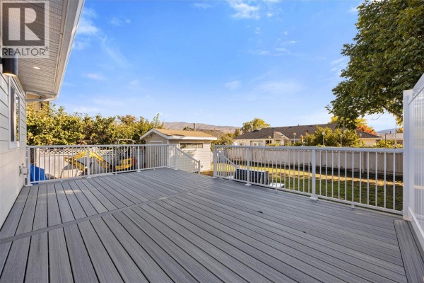 Large composite deck with white railings overlooks a green lawn and distant houses under a blue sky. - 4141 San Clemente Avenue, Peachland