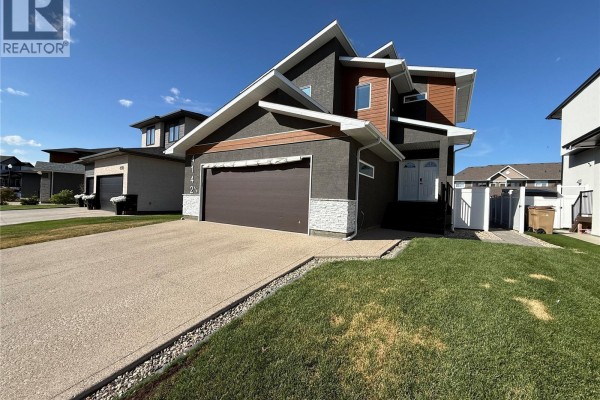 Side view of a modern house with a double garage, green lawn, and paved driveway. - 4142 A/b Green Olive Way E, Regina