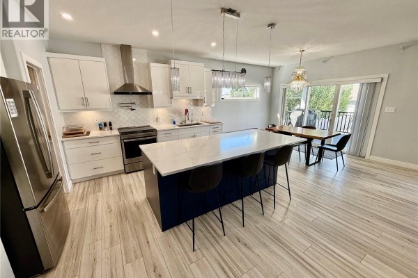Open-concept kitchen with white cabinets, stainless steel appliances, quartz island, and dining area. - 4142 A/b Green Olive Way E, Regina