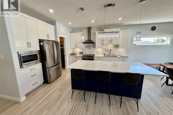 Kitchen featuring white high-gloss cabinets, stainless steel appliances, a large island, and light wood flooring. - 4142 A/b Green Olive Way E, Regina
