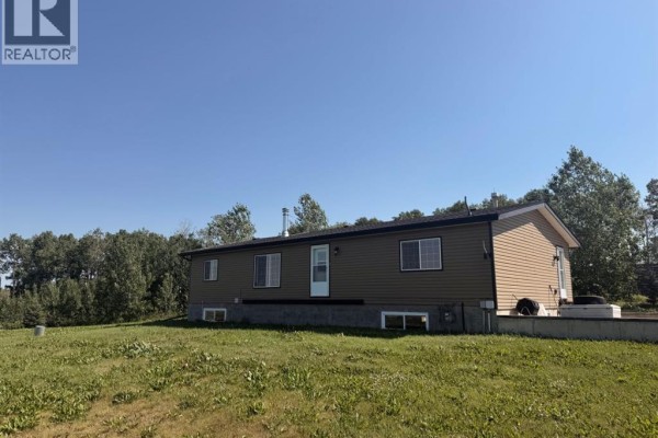 View of the back and side of a brown house situated on a large grassy field with a distant view. - 4142 Township Road 290, Rural Mountain View County