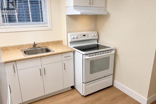 Compact kitchen with white cabinets, a stainless steel sink, and white stove. - 4147 W13th Ave, Vancouver