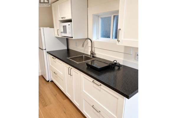 Kitchenette with white cabinets, a black speckled countertop, and a refrigerator. - 4147 W13th Ave, Vancouver