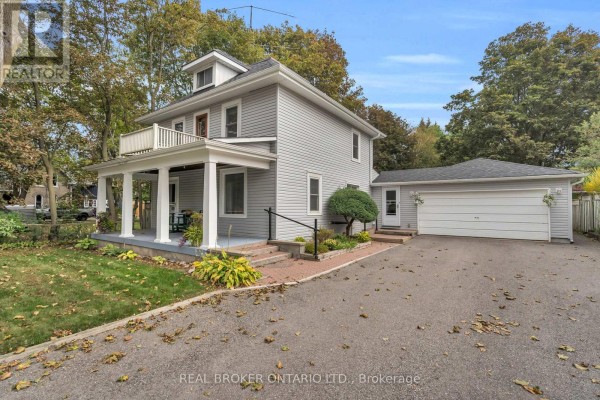 View of a grey house with a covered front porch, white railing balcony, and a detached garage. - 4149 Front Street, Uxbridge