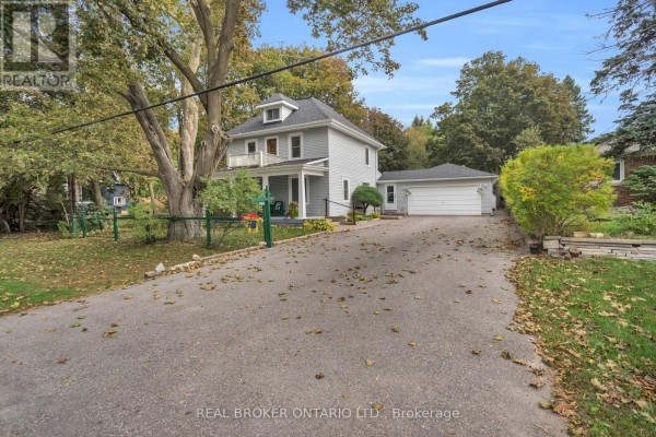 Front exterior of a two-story grey house with a covered porch and a detached garage. - 4149 Front Street, Uxbridge