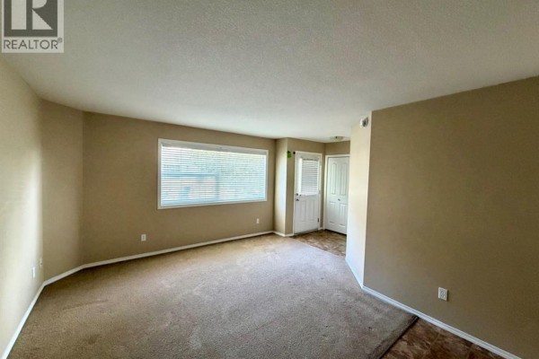 Living room with beige carpet, large window, and tan walls. - 415, 31 Jamieson Avenue, Red Deer
