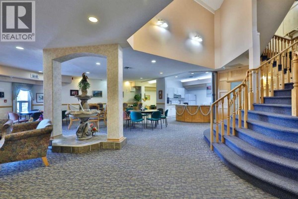 Spacious lobby with blue carpet, curved staircase with wooden railings, and a small fountain. - 415, 4623 65 Street, Camrose