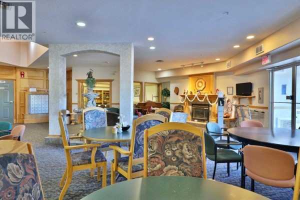 Common area with round tables, chairs, a fireplace with mantel, and a piano. - 415, 4623 65 Street, Camrose