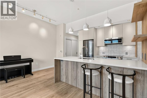 Kitchen island with white countertop, black bar stools, and modern pendant lights, adjacent to a digital piano. - 415 1588 North Dairy Rd, Saanich