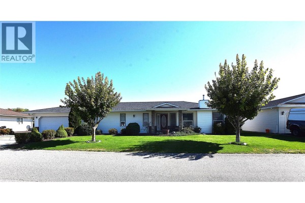 Front exterior view of a white single-story house with a covered entrance and two trees in the yard. - 415 4 Street, Vernon