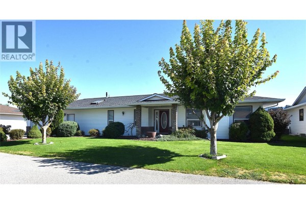 Front exterior view of a white single-story house with a covered entrance and two trees in the yard. - 415 4 Street, Vernon