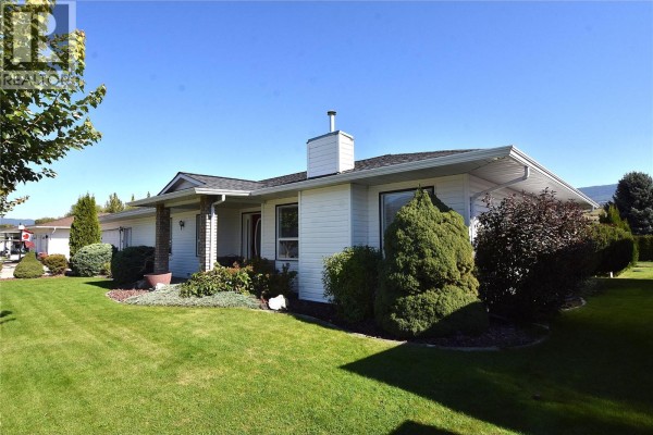 Side exterior view of a white single-story house with a chimney and manicured shrubs. - 415 4 Street, Vernon
