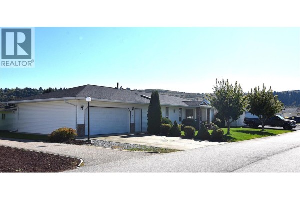 Exterior view of a white single-story house with attached garage and parked vehicles on the street. - 415 4 Street, Vernon