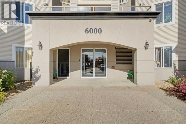 Close-up of the building entrance at 6000 Somervale Court SW with glass doors and beige facade. - 416, 6000 Somervale Court Sw, Calgary