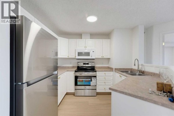 Modern kitchen with white cabinets, stainless steel appliances, and a beige countertop. - 416, 6000 Somervale Court Sw, Calgary