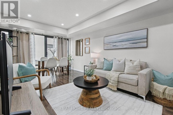 Living room with a sofa, coffee table, rug, and dining area view. - 416 - 130 Widdicombe Hill Boulevard, Toronto