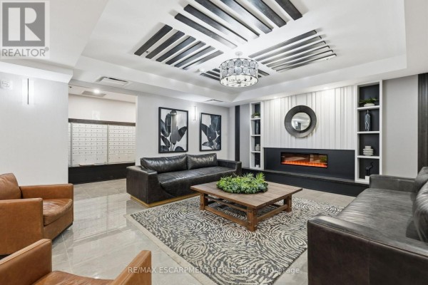Apartment building lobby with dark leather sofas, a fireplace, and patterned rug. - 416 - 870 Queenston Road, Hamilton