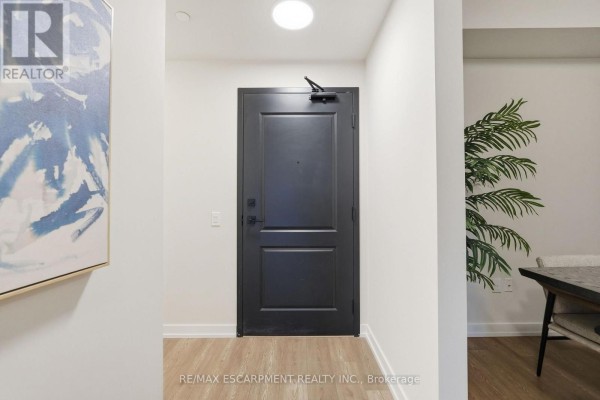 Apartment hallway with a black door, artwork, a plant, and a dining table corner. - 416 - 870 Queenston Road, Hamilton