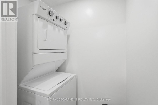 Close-up of stacked white Whirlpool washer and dryer units in a small room. - 416 - 870 Queenston Road, Hamilton