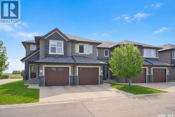 Open concept kitchen and living area with a stainless steel refrigerator, island, dining table, and sofa. - 416 1303 Paton Crescent, Saskatoon