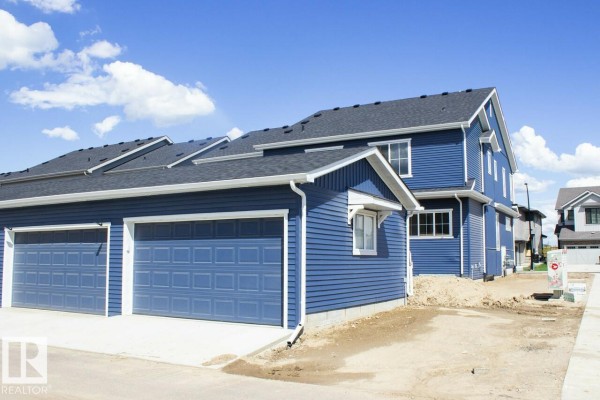 Side exterior view showing attached garages with blue siding and dark gray roofs. - 416 26 St Sw, Edmonton