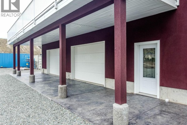 Covered walkway with maroon columns, two white garage doors, and a glass-paned door on a burgundy building. - 416 Hollis Road, Ashcroft